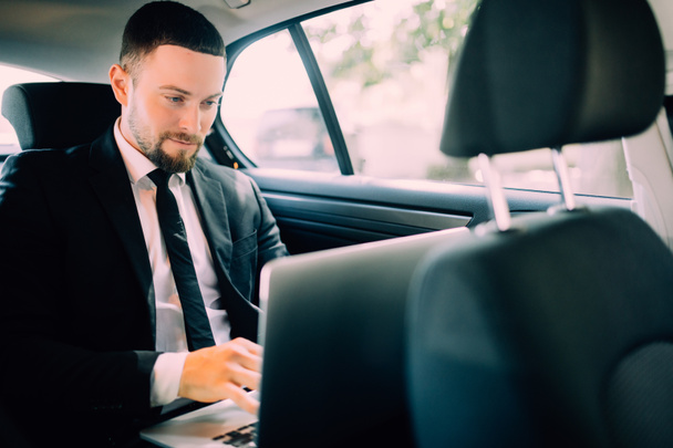 Hombre de negocios guapo sentado con portátil en el asiento trasero del coche
 - Foto, imagen