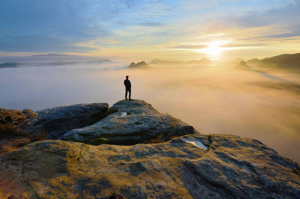 渓谷の上の岩の端にハイカー。明るい朝の太陽に朝霧と紅葉谷人の時計. - 写真・画像