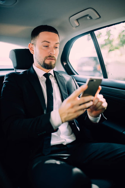A businessman while traveling by car in the back seat, send a message or email and calls. The man in the driver career for his business trips. - Photo, Image