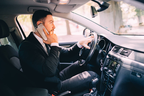 Handsome young businessman talking on his smart phone and smiling while sitting on the front seat - Photo, Image