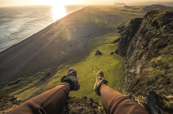 Benen van de toerist in het bijhouden van schoenen en een uitzicht op zwarte zand strand in IJsland - Foto, afbeelding