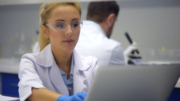 Smart female scientist in safety glasses typing on computer - Video, Çekim