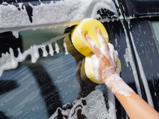 Woman hand with yellow sponge washing car - 写真・画像
