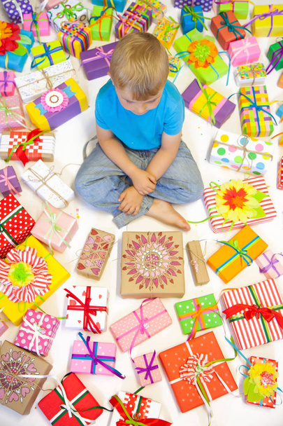 The child is littered with gifts. The boy sits on the floor, and - 写真・画像