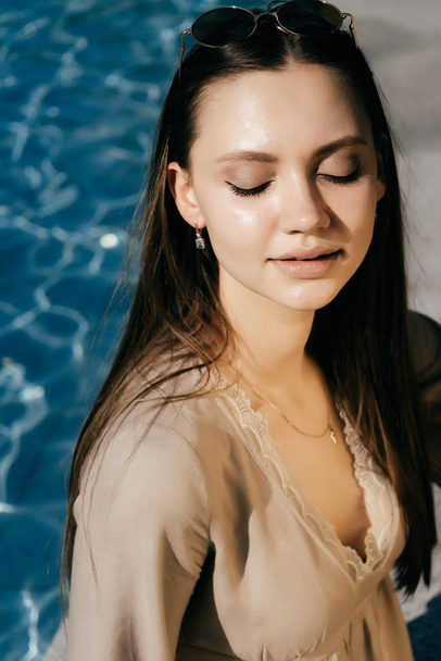 Young fashionable woman sitting near pool, smiling with closed eyes - Foto, afbeelding