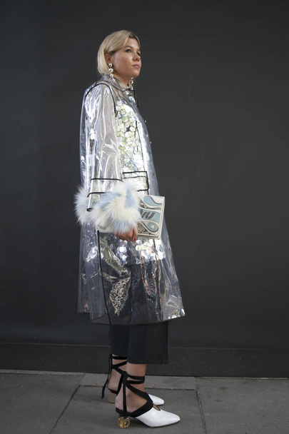 A woman in a transparent raincoat, a silver shirt with paillettes, a clutch, white shoes with golden round heels - Fotó, kép