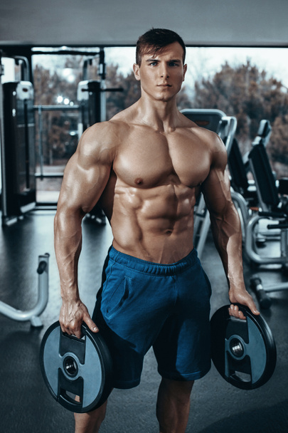Portrait of a handsome man resting near bar in fitness gym and looking at the camera - 写真・画像