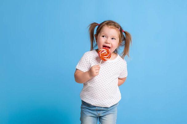 Beautiful little female child holding huge lollipop spiral candy smiling happy isolated on blue background. - Φωτογραφία, εικόνα