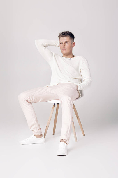 handsome young man in white sweater sits on a chair on - Fotografie, Obrázek