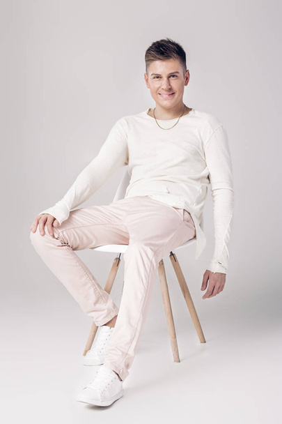 handsome young man in white sweater sits on a chair on - Photo, Image