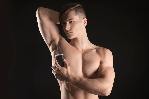Handsome young man with deodorant on dark background - Fotografie, Obrázek