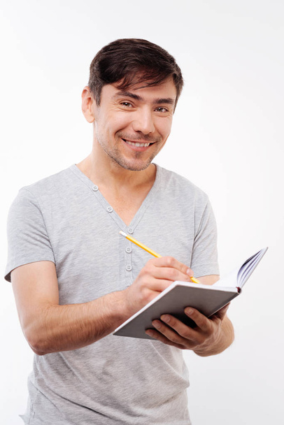 Pleasant bristled man making notes in notebook - Photo, Image