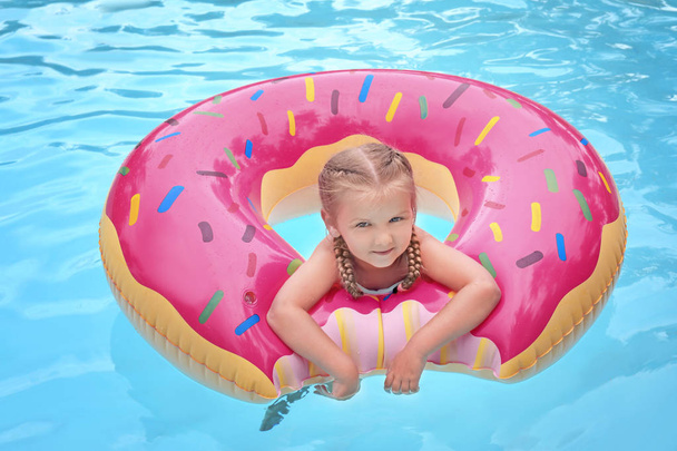 Cute little girl with inflatable donut in swimming pool - Фото, зображення