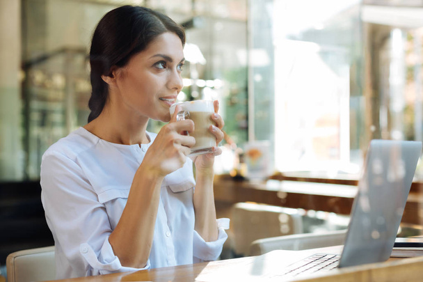 Charming dark-haired woman drinking latte in cafe - 写真・画像