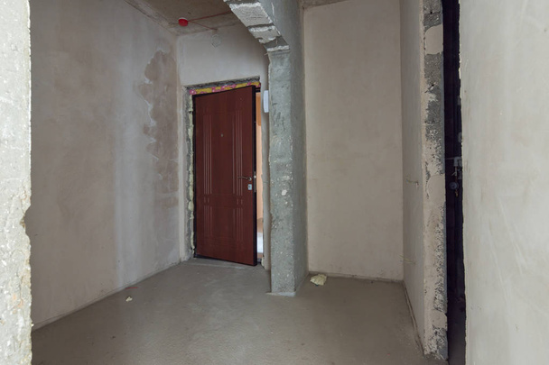 A entrada para o apartamento é um novo edifício, a porta da frente e paredes de concreto nu e rebocadas
 - Foto, Imagem