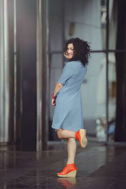 an adult curly woman, brown eyes and a blue dress at the business center, cheerful and fervent - Valokuva, kuva