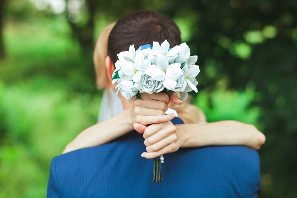The bride is hugging the groom by the neck. A girl is holding a wedding bouquet - Foto, imagen