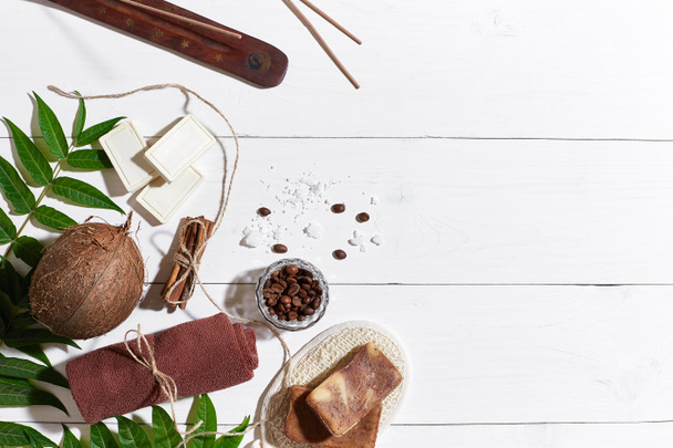 Natural handmade soaps with coffee beans, cinnamon, sea salt, loofah, brown towel, coconut and green leaves on white wooden background - Photo, Image
