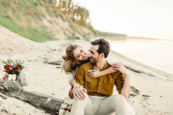 A young couple is smiling and hugging on the beach. Beautiful girl embrace her boyfriend from back. Wedding walk. Artwork - Photo, Image