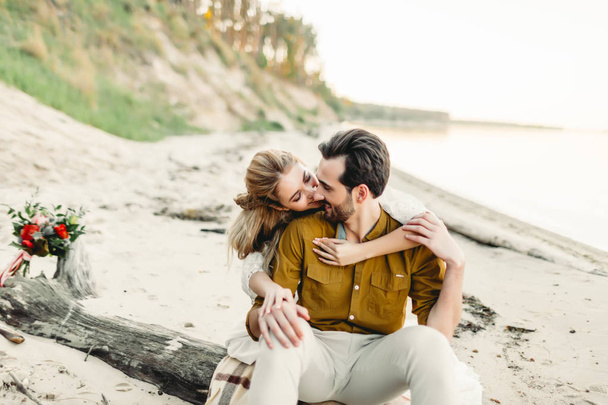 A young couple is hugging on the beach. Beautiful girl embrace her boyfriend from back. Wedding walk. A newlyweds looks at each other. Artwork - Photo, Image