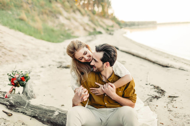 A young couple is smiling and hugging on the beach. Rustic wedding ceremony outdoors. Bride and groom look at each other with tenderness and love. Artwork - Photo, Image
