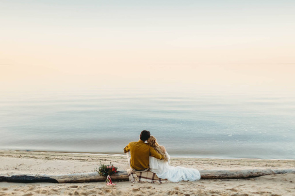 Een mooi paar is zittend op het logboek en kijk naar de zee. Romantische datum op het strand. Uitzicht vanaf de achterkant. Bruiloft. Illustraties - Foto, afbeelding
