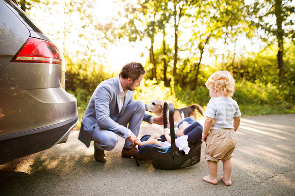 Young father with baby and toddler by the car. - Photo, image