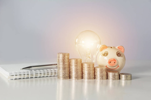 Energy saving light bulb with piggy bank and stacks of coins on table. Financial and saving concept. - Photo, Image