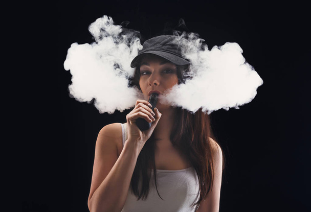 Young woman vaping e-cigarette with smoke on black - Fotó, kép