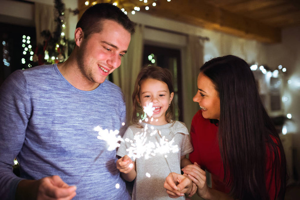 Young family with sparklers at Christmas time at home. - Фото, зображення