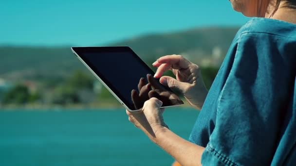 Κοντινό πλάνο του μια γυναίκα πενήντα χρησιμοποιώντας tablet στην ακτή της θάλασσας. - Πλάνα, βίντεο