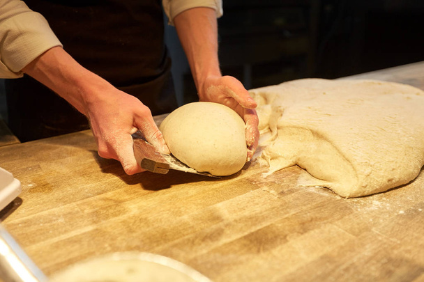 baker portioning dough with bench cutter at bakery - Zdjęcie, obraz