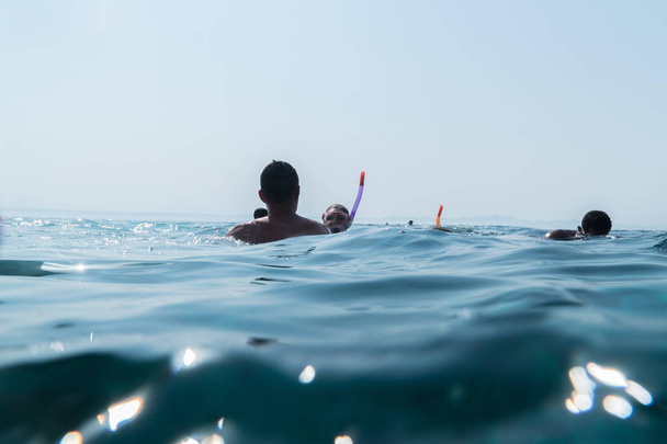 As pessoas nadam na superfície da água em máscaras com tubos e olham para o recife de coral.
 - Foto, Imagem