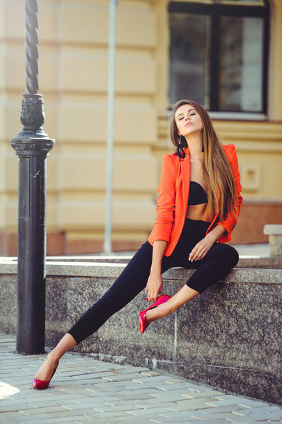 Muoti kaunis nainen punainen takki ja musta rintaliivit ja housut kaupungin taustalla
 - Valokuva, kuva