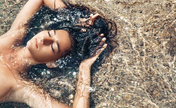 mooie jonge vrouw in water op het strand liggen - Foto, afbeelding