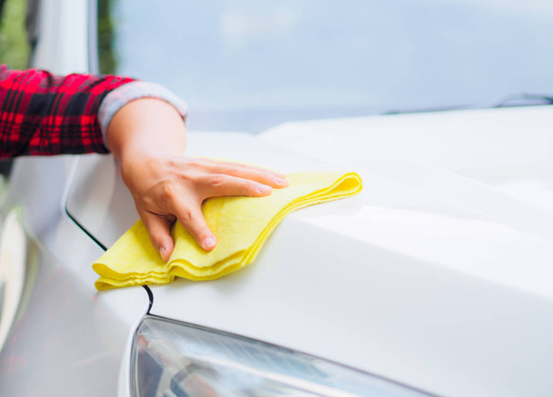 Hand with yellow microfiber cloth cleaning white car. - Foto, immagini