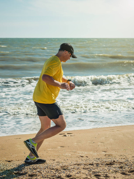 The man in the baseball cap and yellow shirt performs a workout on the ocean. - Foto, Bild