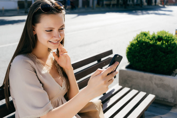 A girl sits on a bench and reads looking good news in the phone - Фото, зображення
