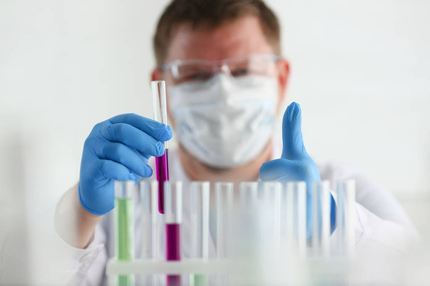 Um químico macho segura um tubo de ensaio de vidro na sua mão transborda
 - Foto, Imagem