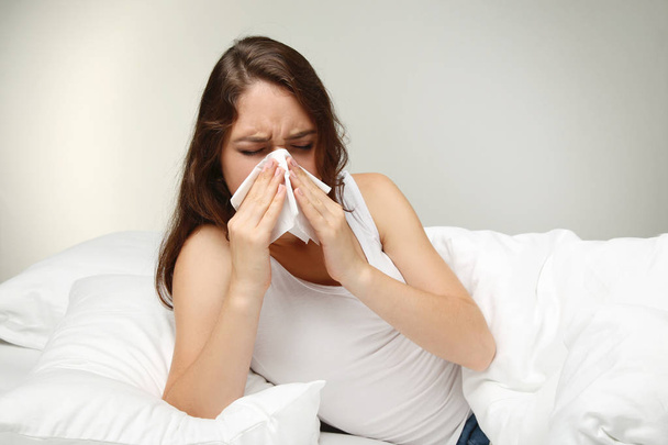 Sick young woman sneezing in tissue in white bed - Foto, immagini
