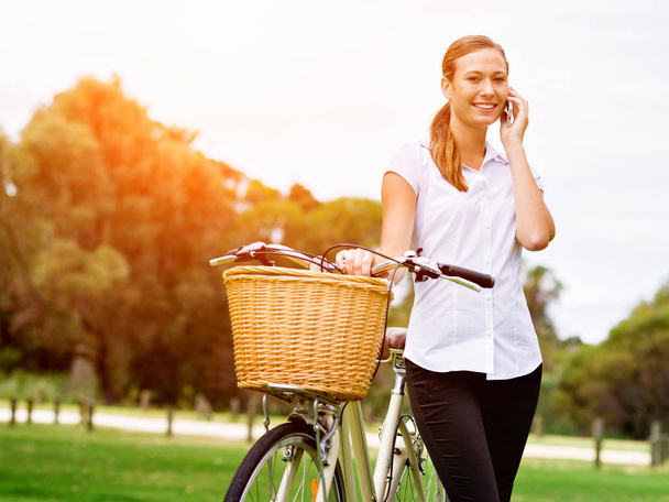 Beautiful young blond woman with bike in park talking over phone - Fotografie, Obrázek