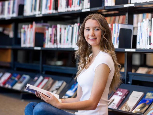 Happy female student holding books at the library - Foto, afbeelding