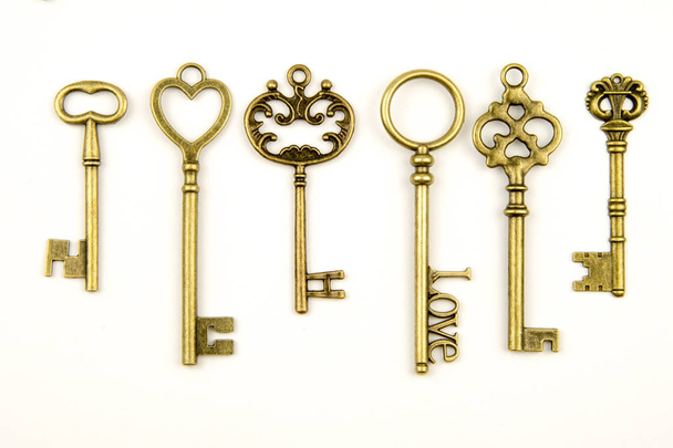 Ornamental medieval vintage keys with intricate forging, composed of fleur-de-lis elements, victorian leaf scrolls and heart shaped swirls. antique golden door key isolated on white background - Fotó, kép