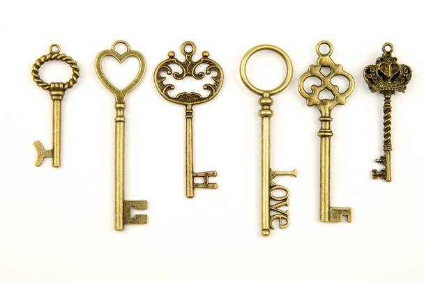Ornamental medieval vintage keys with intricate forging, composed of fleur-de-lis elements, victorian leaf scrolls and heart shaped swirls. antique golden door key isolated on white background - Fotó, kép