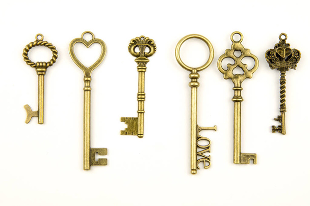 Ornamental medieval vintage keys with intricate forging, composed of fleur-de-lis elements, victorian leaf scrolls and heart shaped swirls. antique golden door key isolated on white background - Photo, Image