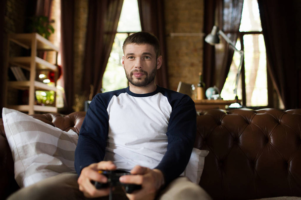 View of young man sitting on couch holding game controller joystick. - Foto, Imagem