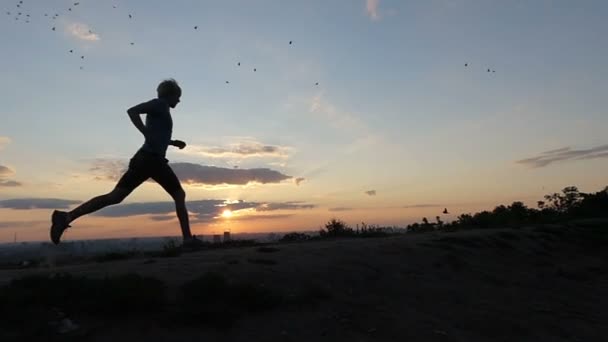 Молода людина працює швидко в деяких горбистій місцевості на заході сонця в Slo-Mo - Кадри, відео