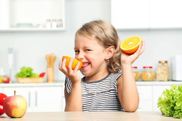 Little girl with oranges sitting in the kitchen - Fotó, kép