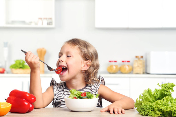 Little girl eating salad in the kitchen - Fotó, kép
