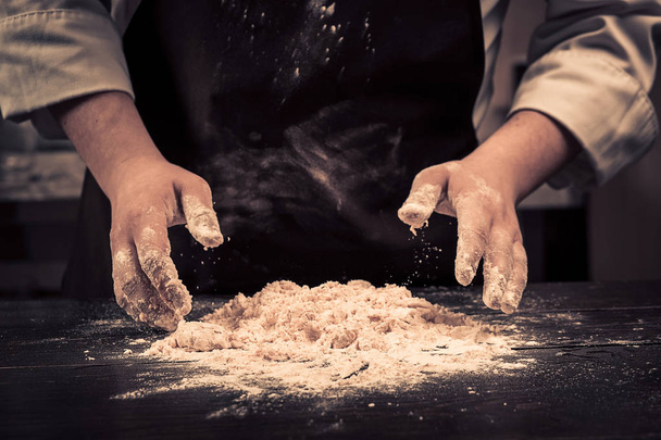 De chef-kok maakt deeg voor de pasta op een houten tafel - Foto, afbeelding